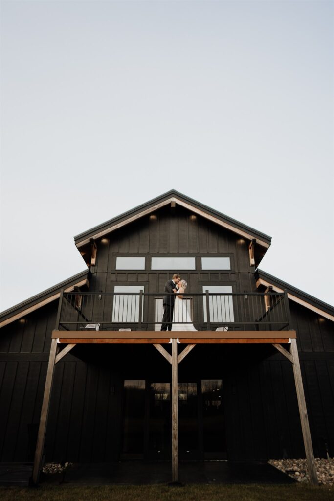 Bride and Groom standing on balcony at Ivy Black looking out into the field 