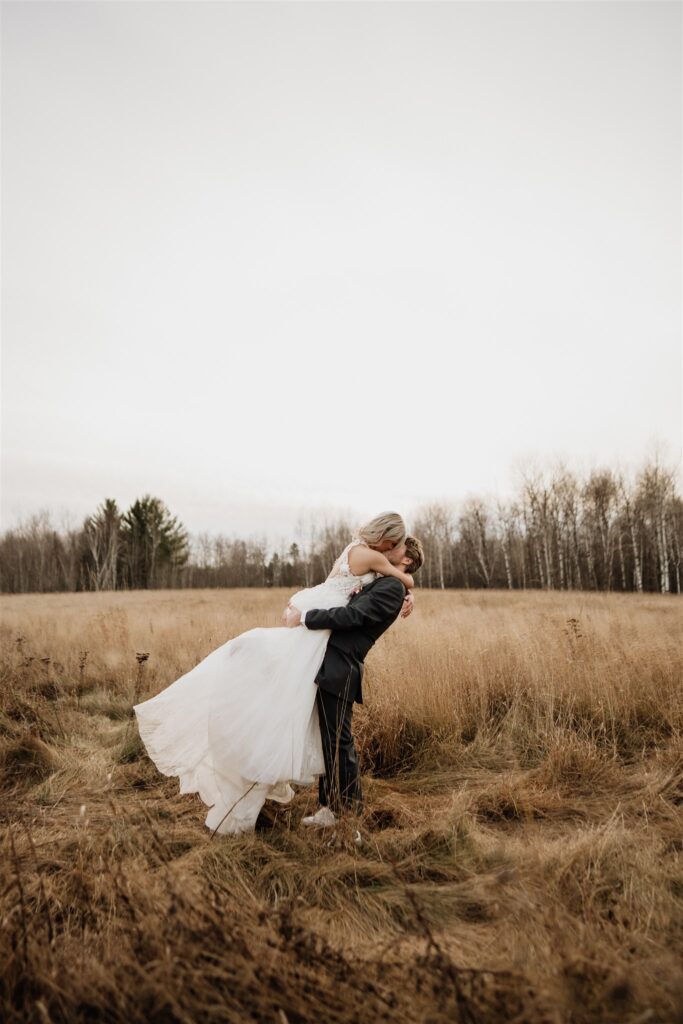 groom picking up bride in grassy field at ivy black 