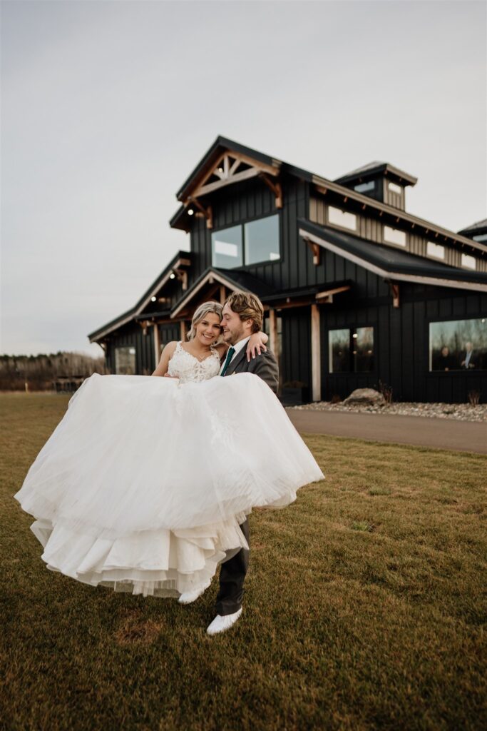 groom picking bride up and spinning her with Ivy black wedding venue behind them