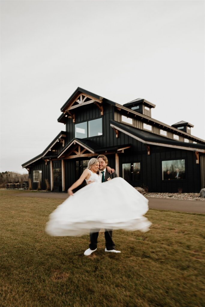 groom picking bride up and spinning her with Ivy black wedding venue behind them